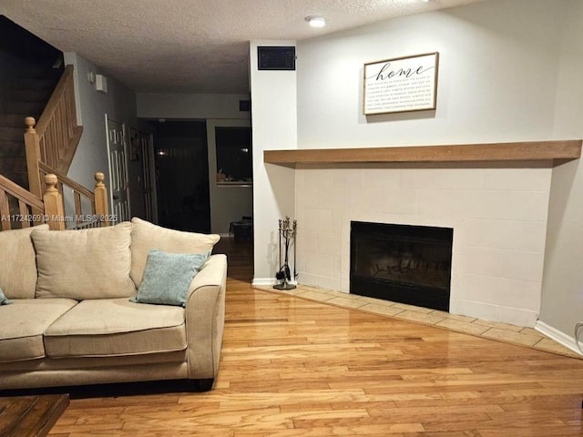 living room with a tiled fireplace, hardwood / wood-style floors, and a textured ceiling