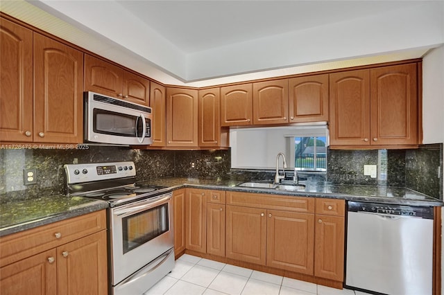 kitchen with dark stone countertops, stainless steel appliances, sink, light tile patterned flooring, and tasteful backsplash