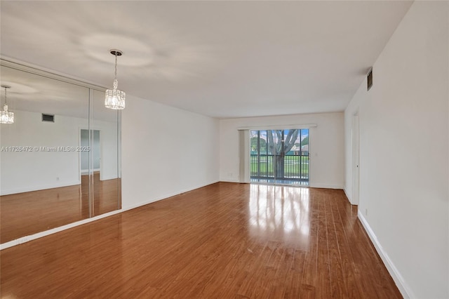 spare room with an inviting chandelier and wood-type flooring