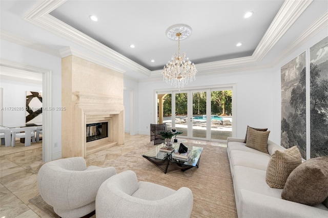 living room with a premium fireplace, ornamental molding, an inviting chandelier, and a tray ceiling