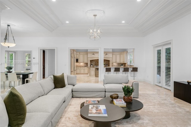 living room featuring plenty of natural light, a tray ceiling, a chandelier, and ornamental molding