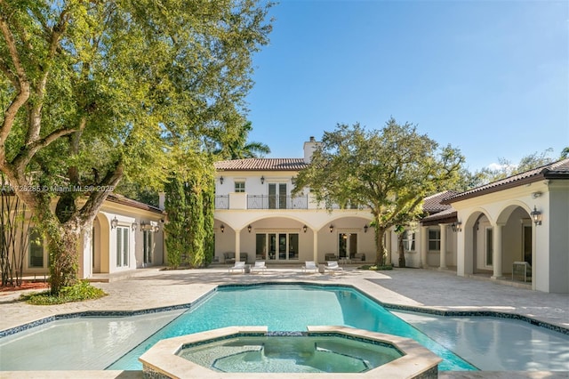 back of property with a swimming pool with hot tub, french doors, a balcony, and a patio