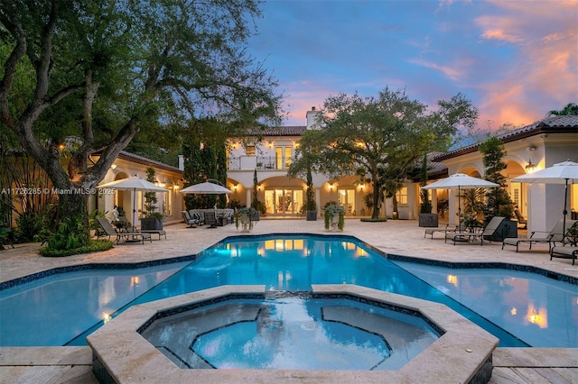 pool at dusk featuring a patio area and an in ground hot tub