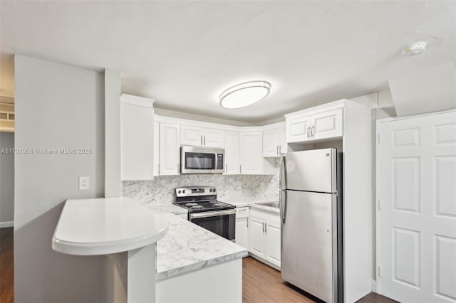 kitchen featuring stainless steel appliances, light wood-type flooring, kitchen peninsula, white cabinets, and backsplash