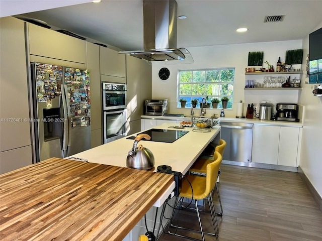 kitchen with wood-type flooring, island exhaust hood, sink, stainless steel appliances, and white cabinets