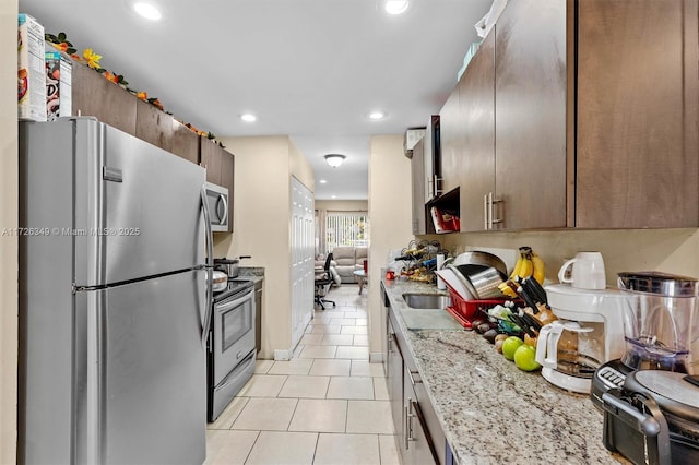 kitchen with appliances with stainless steel finishes, dark brown cabinets, light stone counters, and light tile patterned floors