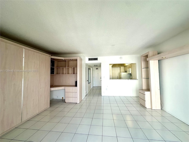 unfurnished living room with a textured ceiling, light tile patterned flooring, and built in desk