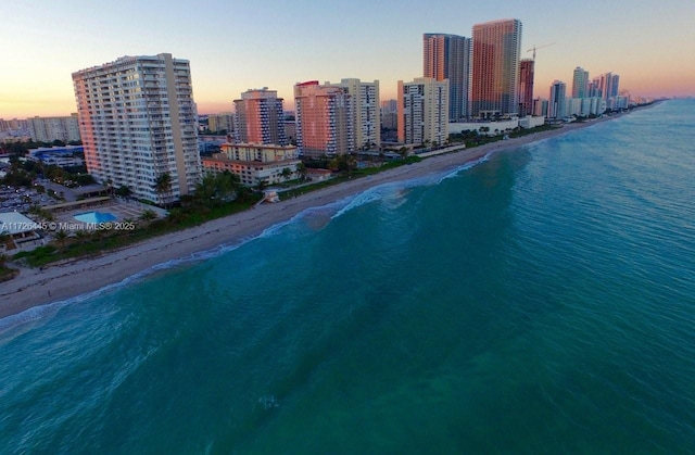 aerial view at dusk featuring a view of the beach and a water view