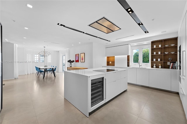 kitchen featuring sink, white cabinets, black electric cooktop, a center island with sink, and wine cooler