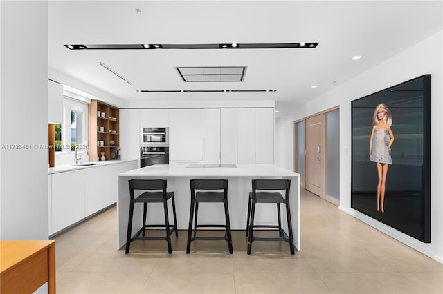 kitchen featuring sink, white cabinetry, a kitchen breakfast bar, light tile patterned floors, and a kitchen island