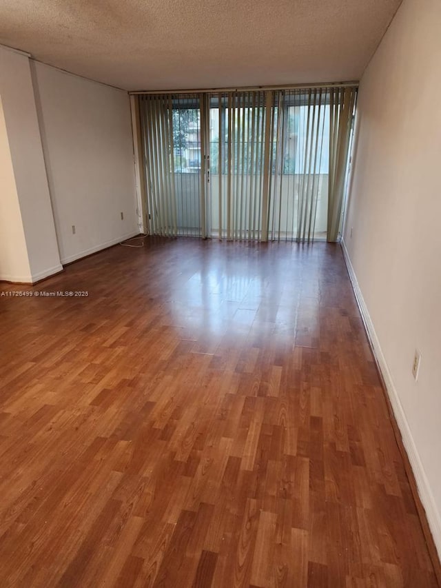 spare room featuring a textured ceiling, a wall of windows, and hardwood / wood-style floors