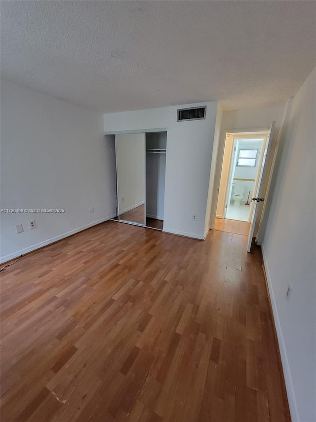 unfurnished bedroom with a textured ceiling, a closet, and hardwood / wood-style flooring