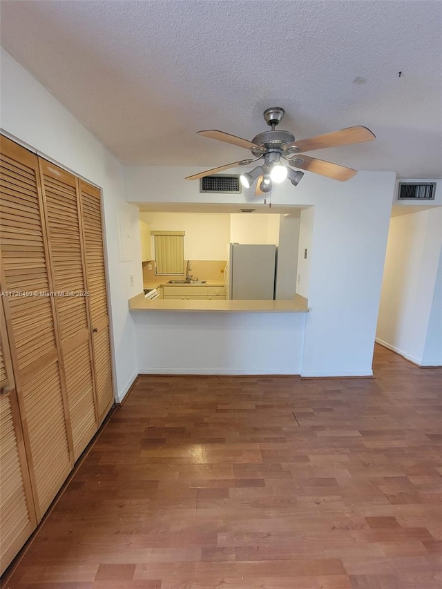 unfurnished living room with ceiling fan, sink, a textured ceiling, and hardwood / wood-style floors