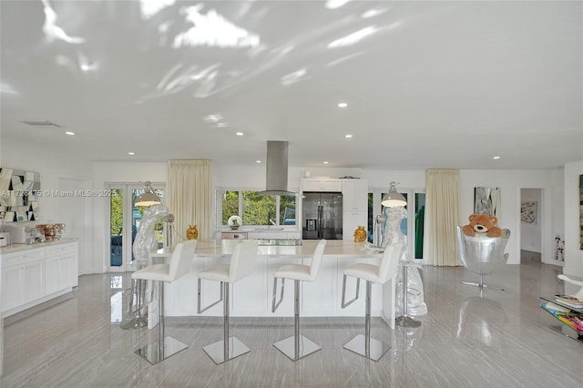 kitchen featuring white cabinetry, island exhaust hood, black fridge, and a kitchen bar