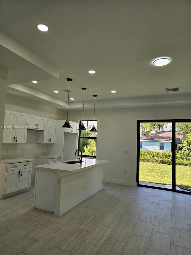 kitchen with a center island with sink, pendant lighting, a tray ceiling, sink, and white cabinetry