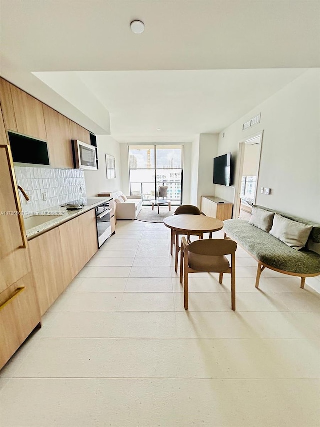 kitchen featuring sink, light brown cabinets, backsplash, light stone countertops, and stainless steel microwave