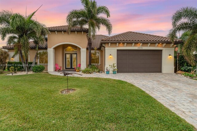 mediterranean / spanish-style home featuring a garage, a lawn, and french doors