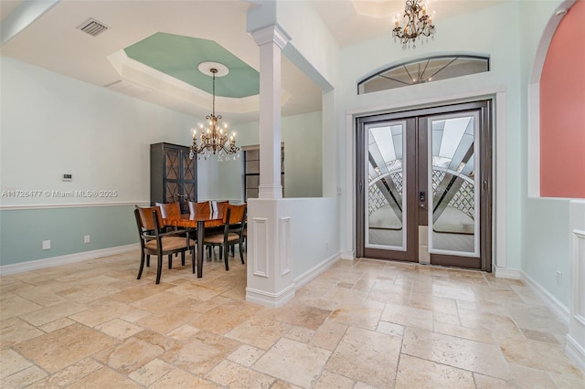 entryway featuring french doors, ornate columns, a tray ceiling, and a notable chandelier