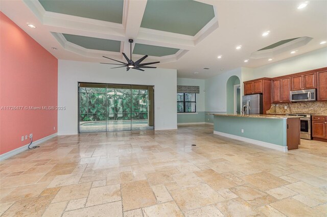 kitchen with appliances with stainless steel finishes, decorative backsplash, coffered ceiling, ceiling fan, and a center island with sink