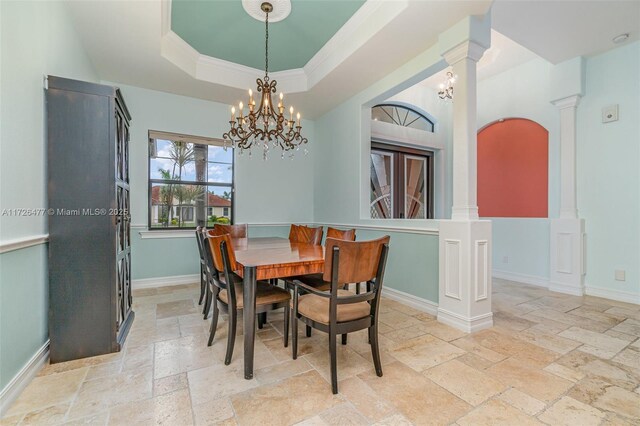 dining room featuring an inviting chandelier, ornamental molding, a raised ceiling, and ornate columns