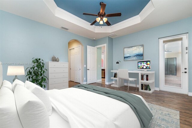 bedroom with dark wood-type flooring, ceiling fan, ornamental molding, and a raised ceiling