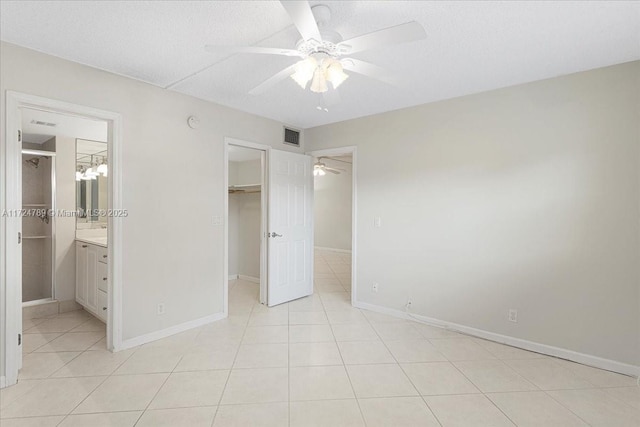 unfurnished bedroom featuring ensuite bath, a spacious closet, a closet, light tile patterned floors, and ceiling fan