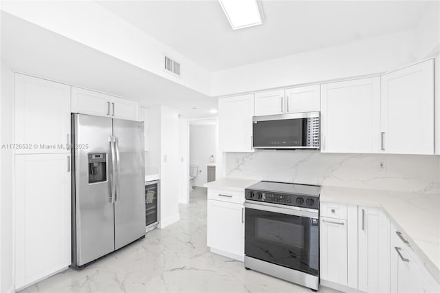 kitchen with wine cooler, appliances with stainless steel finishes, light stone countertops, white cabinets, and backsplash