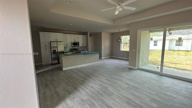 kitchen with a tray ceiling, white cabinetry, appliances with stainless steel finishes, and a center island with sink