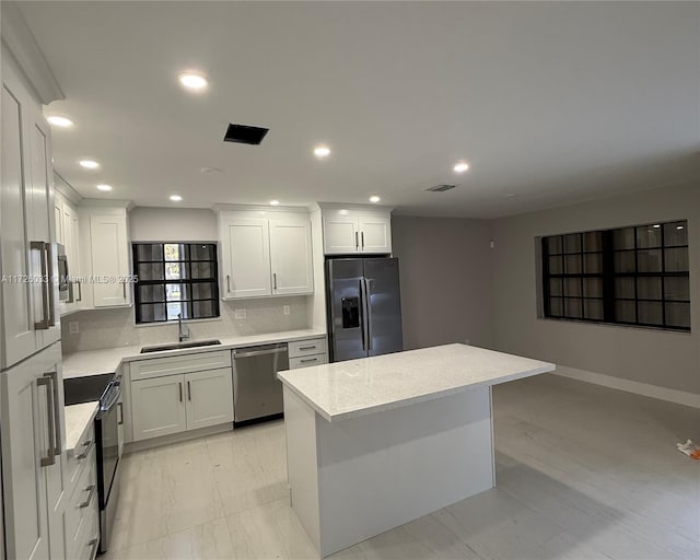 kitchen featuring appliances with stainless steel finishes, a center island, decorative backsplash, white cabinets, and sink