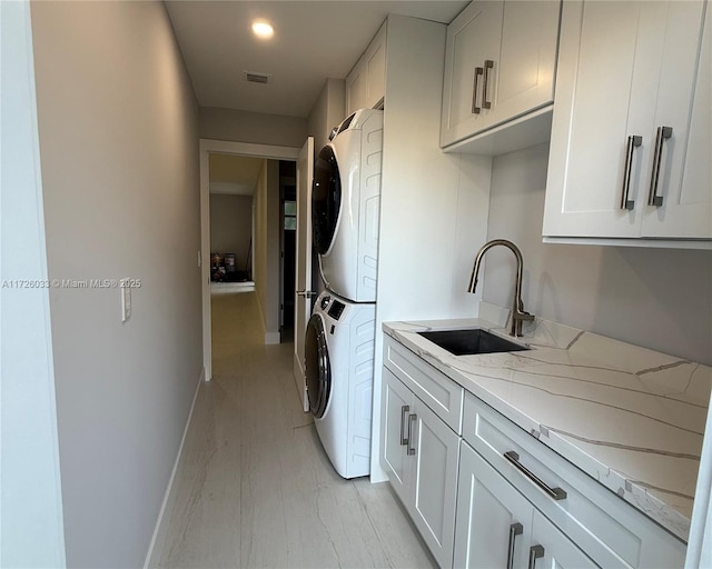 laundry room featuring stacked washer and dryer, cabinets, and sink