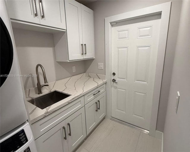 kitchen featuring white cabinets, stacked washer / dryer, light stone countertops, sink, and fridge