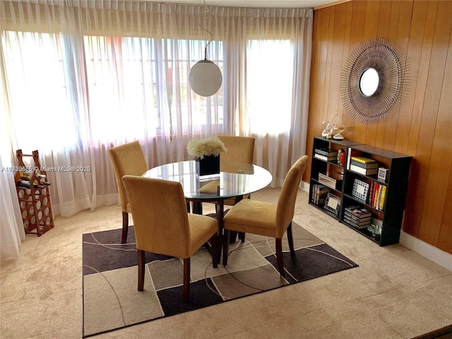 carpeted dining space featuring wooden walls