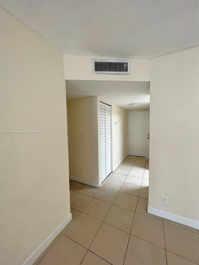 corridor featuring a textured ceiling and light tile patterned floors