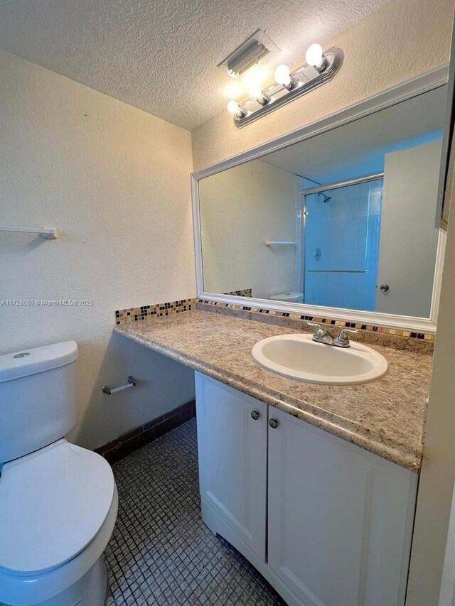 bathroom featuring a textured ceiling, tile patterned flooring, vanity, toilet, and a shower with shower door