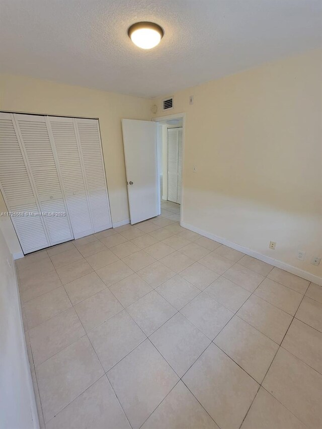 unfurnished bedroom with a textured ceiling, a closet, and light tile patterned floors