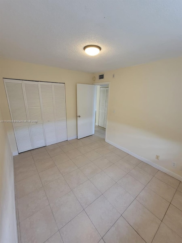 unfurnished bedroom with a textured ceiling, a closet, and light tile patterned floors