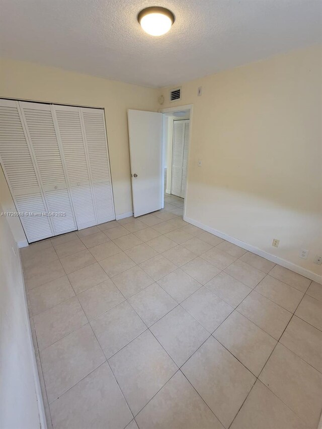 unfurnished bedroom featuring a textured ceiling, a closet, and light tile patterned flooring