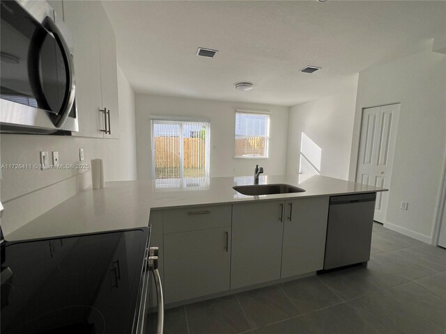 kitchen featuring appliances with stainless steel finishes, kitchen peninsula, light tile patterned floors, white cabinets, and sink