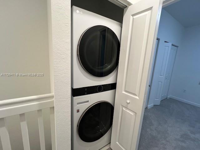 clothes washing area featuring stacked washer and dryer and carpet floors