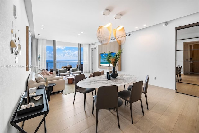 dining room with light hardwood / wood-style floors, a wall of windows, and a water view