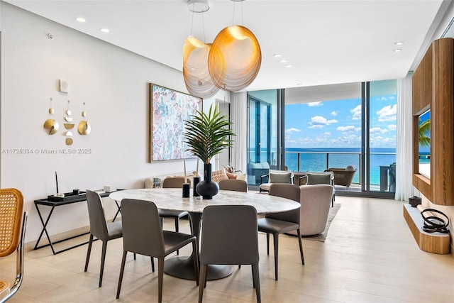 dining area featuring a wall of windows, light wood-type flooring, and a water view