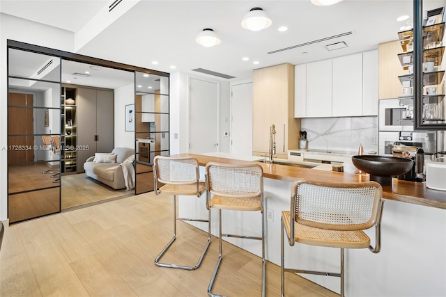 kitchen with a breakfast bar area, light wood-type flooring, decorative backsplash, white cabinets, and sink