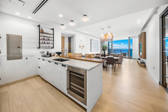 kitchen with light stone counters, kitchen peninsula, wine cooler, white cabinetry, and sink