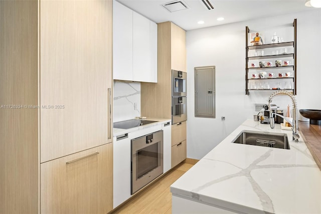 kitchen with sink, white cabinets, electric panel, light stone counters, and backsplash