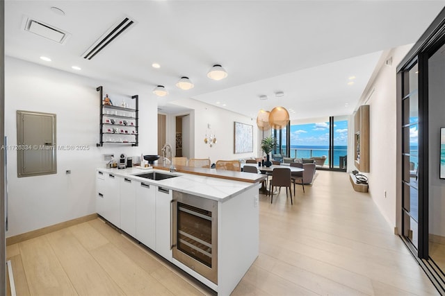 kitchen with kitchen peninsula, a water view, wine cooler, white cabinetry, and sink