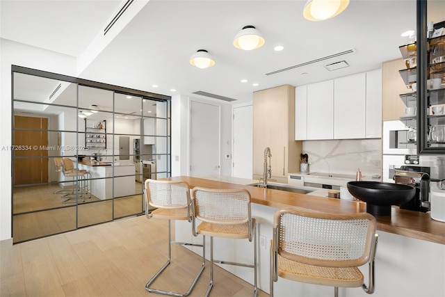 kitchen featuring sink, white cabinetry, a kitchen breakfast bar, tasteful backsplash, and light hardwood / wood-style flooring