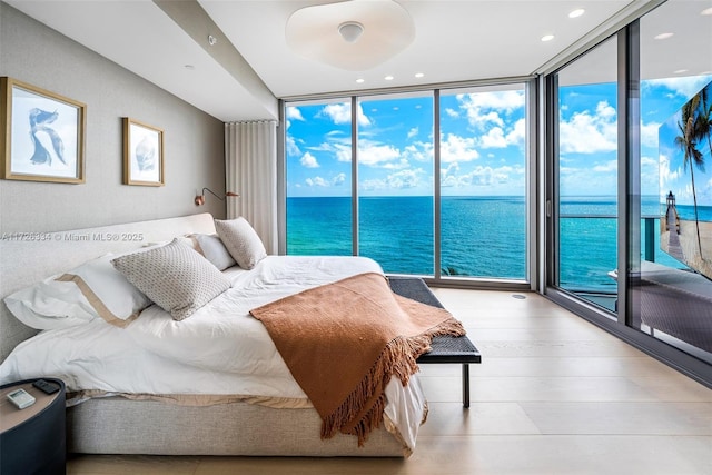 bedroom featuring access to outside, a wall of windows, light hardwood / wood-style flooring, and a water view