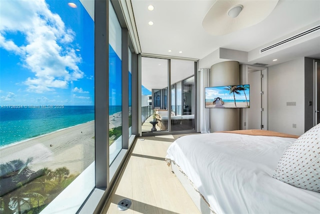 bedroom featuring floor to ceiling windows, a view of the beach, light wood-type flooring, ceiling fan, and a water view