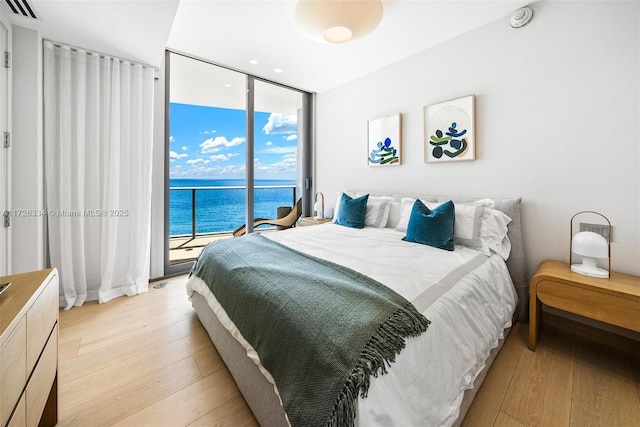 bedroom with a wall of windows, access to exterior, light wood-type flooring, and a water view