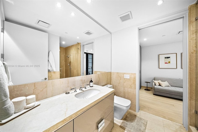 bathroom featuring tile patterned flooring, toilet, walk in shower, vanity, and tile walls